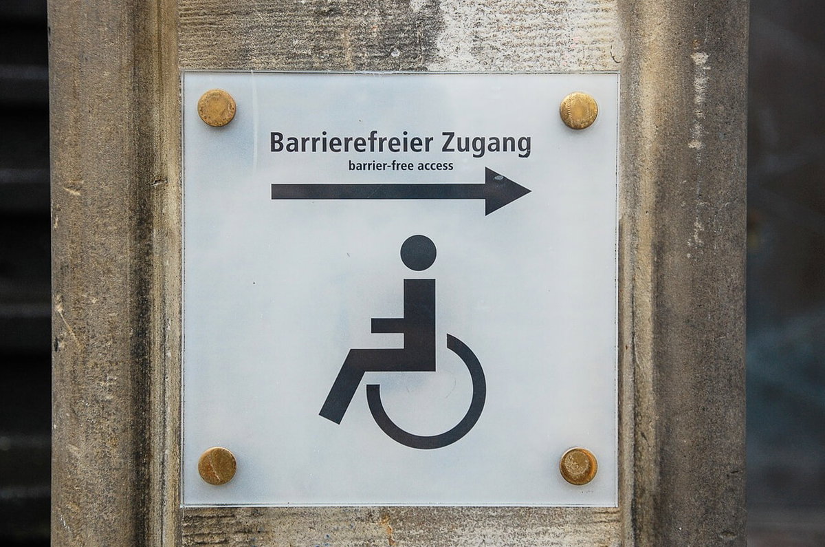 Ein Schild mit einem Rollstuhl, Pfeil und Satz Barrierefreier Zugang