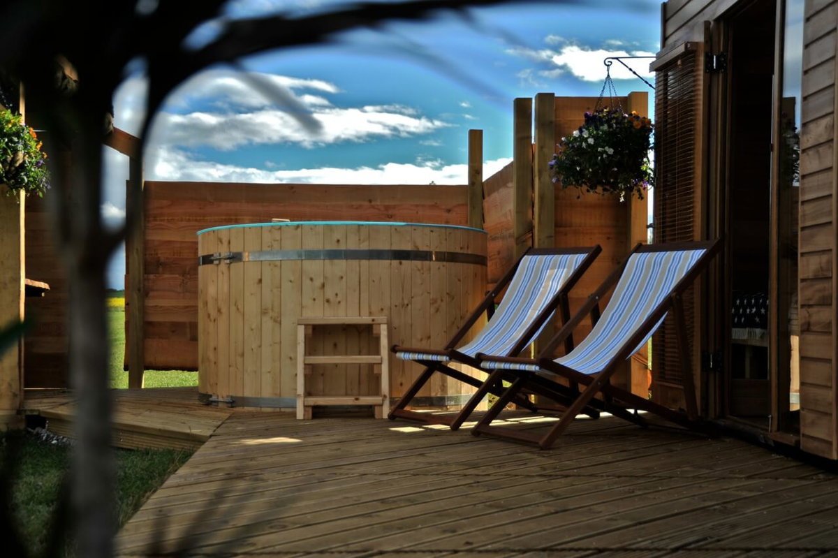 Die Terrasse von einem Tiny House mit Jacuzzi und Liegestuehlen