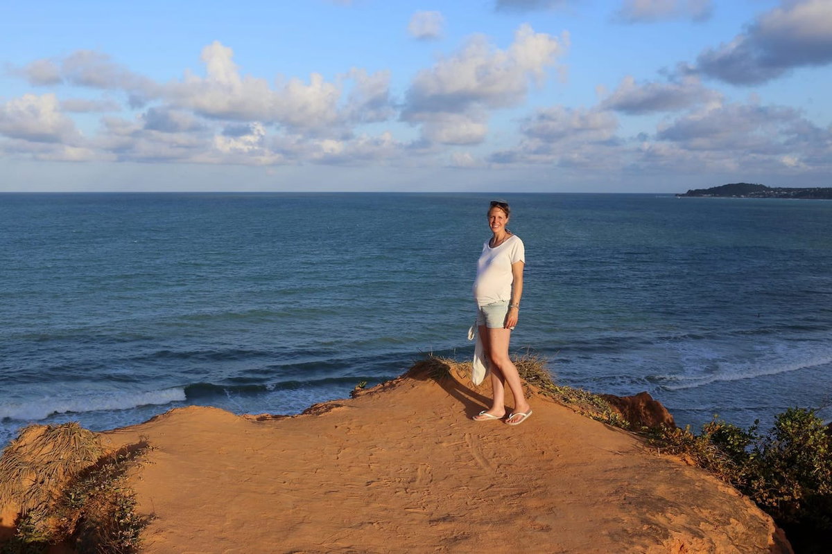 Sabine reist schwanger und steht mit Babybauch am Meer