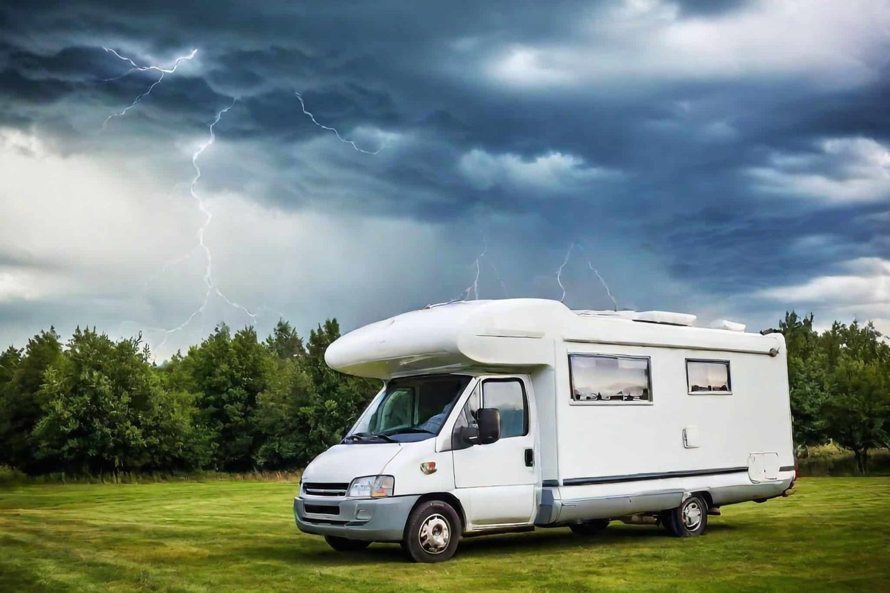 Ein Wohnmobil steht im Gewitter auf einer Wiese, es sind Blitze am Himmel.