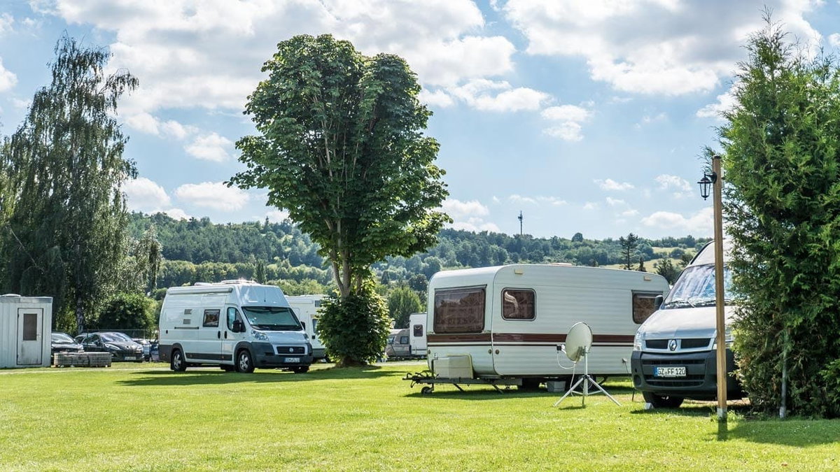 Wohnmobil und Wohnwagen auf einer Wiese. Mit diesen Camping Spartipps kommst du guenstig ans Ziel
