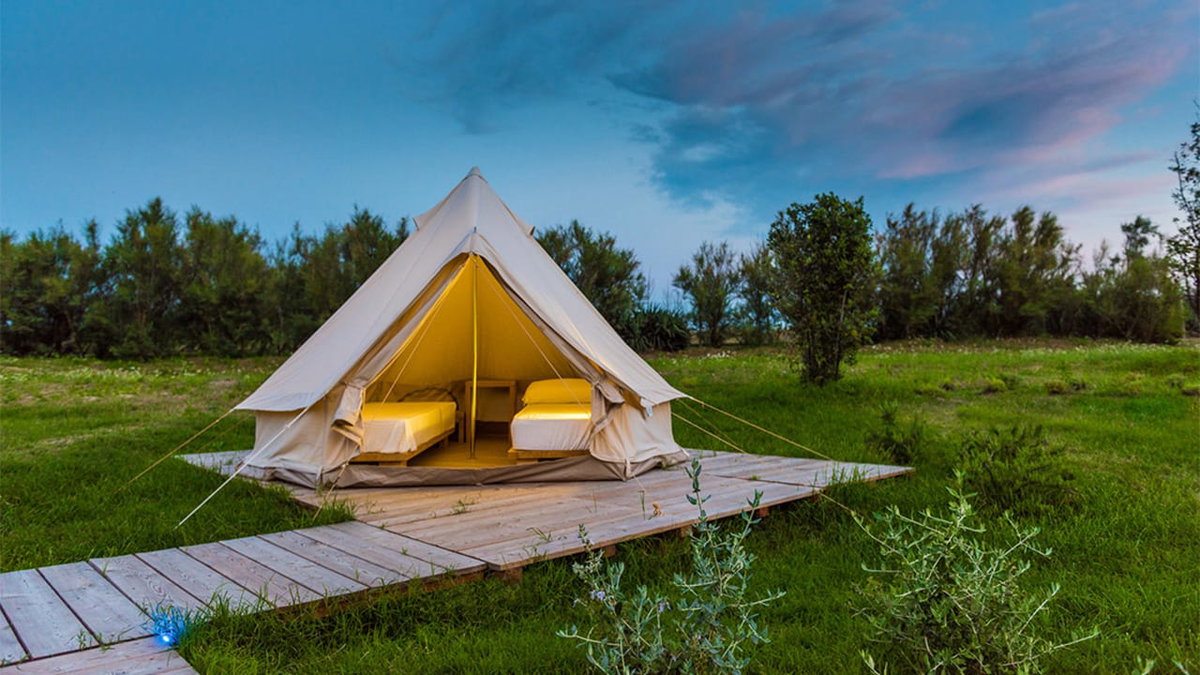 Ein schoenes weisses Zelt auf einer Wiese eines Platzes fuer Glamping in Italien