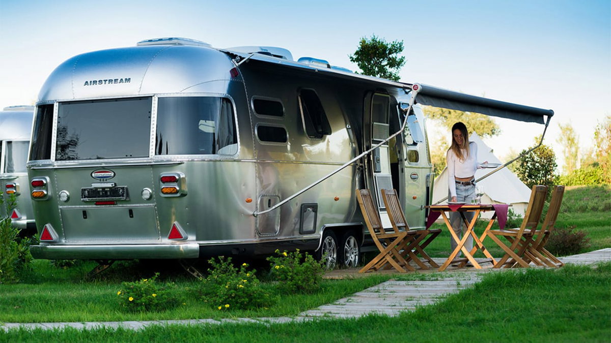 Eine Frau deckt den Tisch vor einem Airstream beim Glamping in Italien