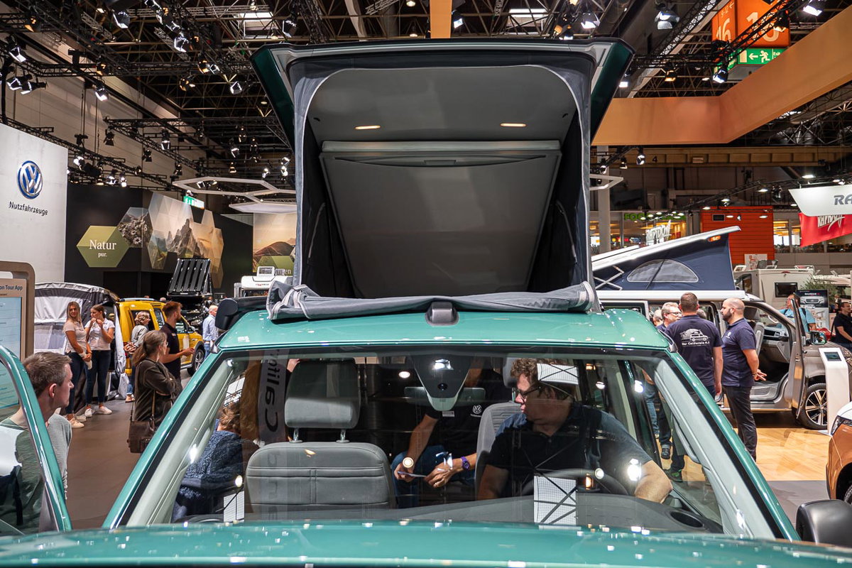 Blick von vorn durch die Windschutzscheibe und auf das geöffnete Hochdach eines VW California 6.1 Coast auf dem Messestand des Caravan Salon 2019 in Düsseldorf
