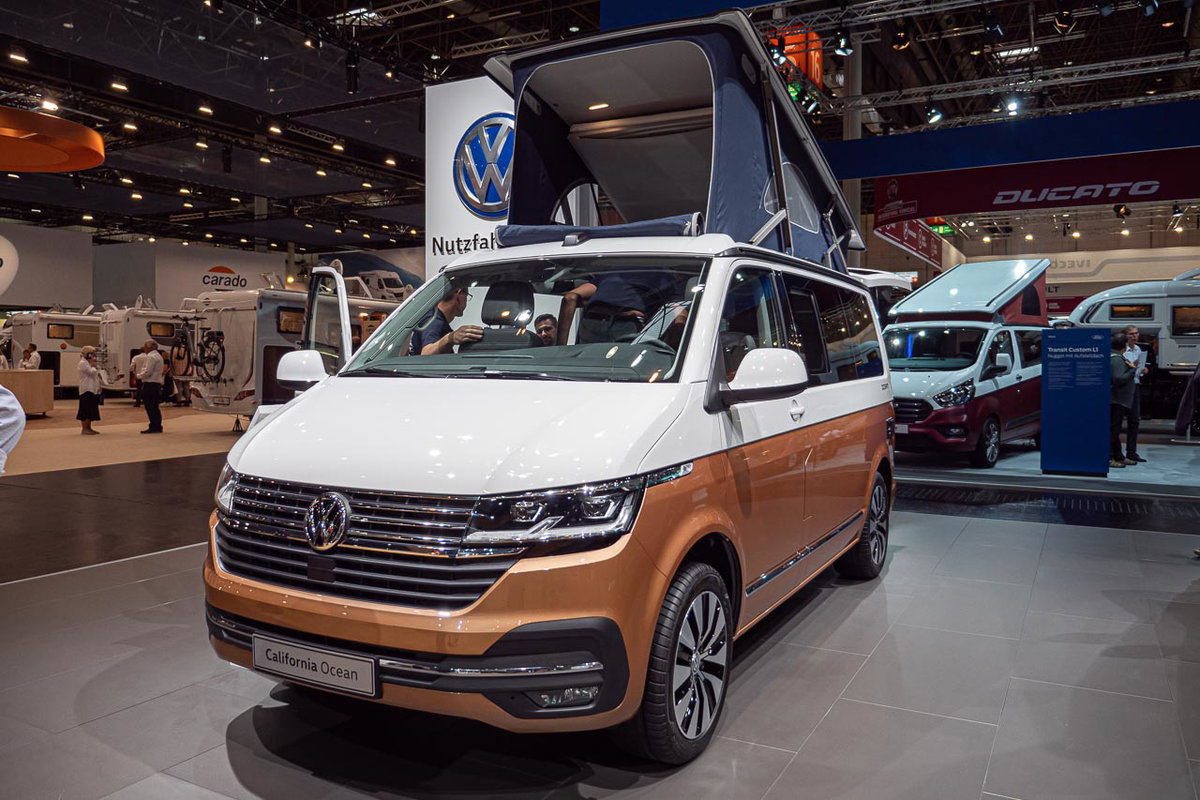 Blick von vorn auf einen VW California 6.1 Ocean mit offener Heckklappe und aufgestelltem Hochdach auf dem Messestand des Caravan Salon 2019 in Düsseldorf