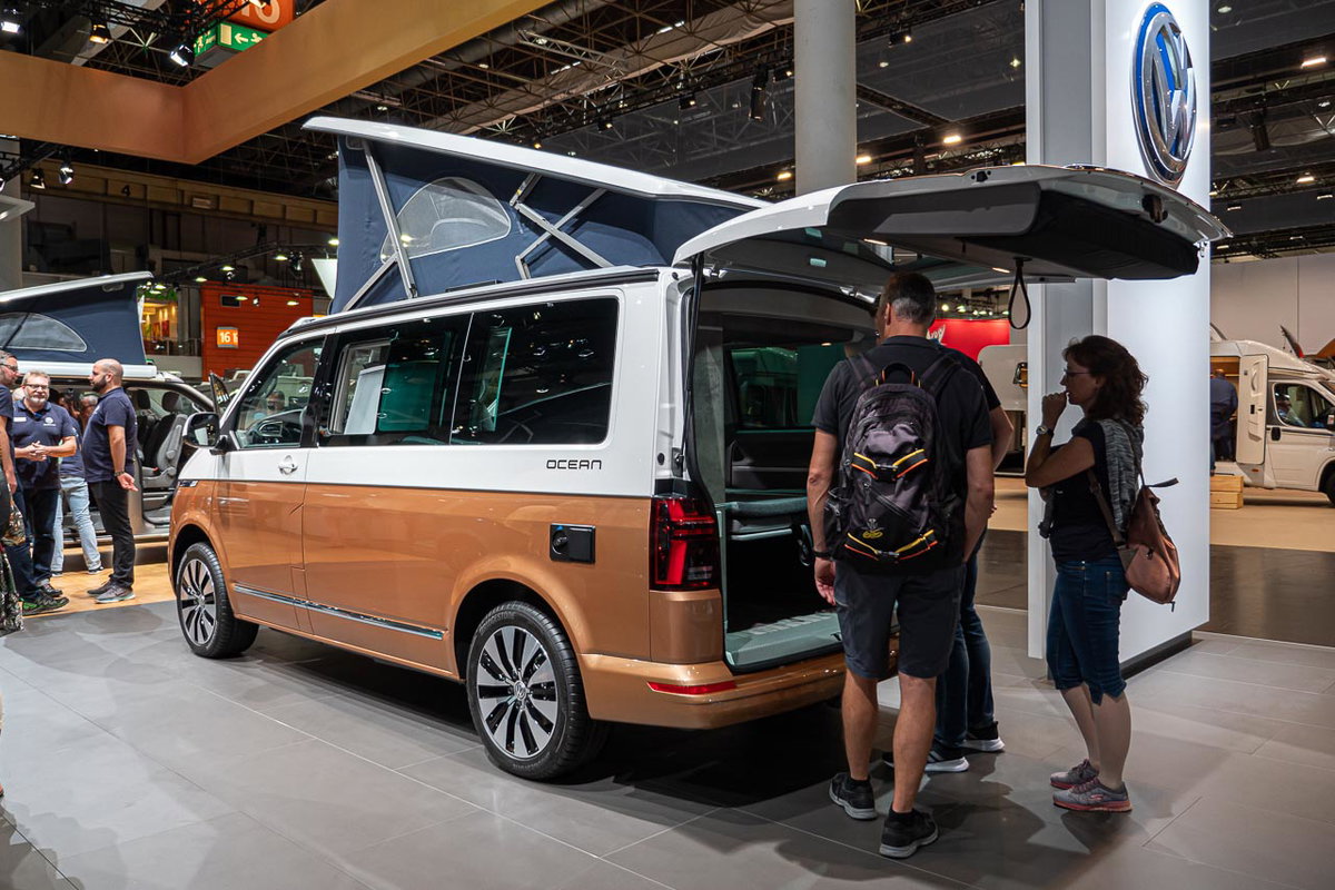 Blick von der Seite auf einen VW California 6.1 Ocean mit offener Heckklappe und aufgestelltem Hochdach auf dem Messestand des Caravan Salon 2019 in Düsseldorf