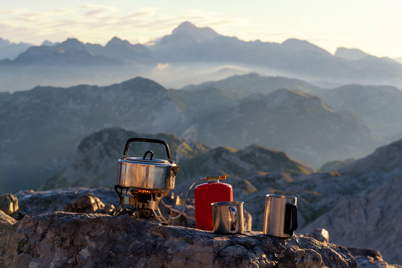 Gaskocher mit Töpfen steht auf einem Felsen mit Ausblick auf Berge