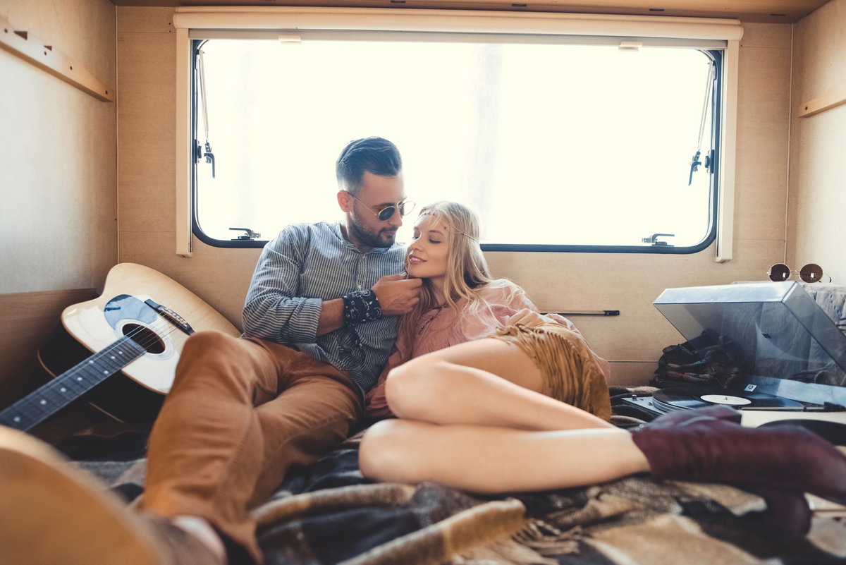 Hippie-Paar umarmt sich im Wohnmobil mit Akustikgitarre und Plattenspieler