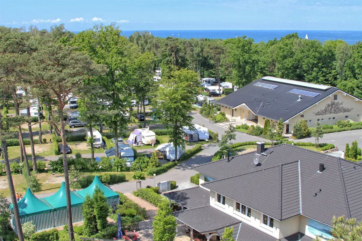 Camping.info Nr. 1 in Deutschland: Campingplatz Kühlungsborn. Zu sehen ist eine Luftaufnahme von einem Campingplatz im Grünen, im Hintergrund das Meer.