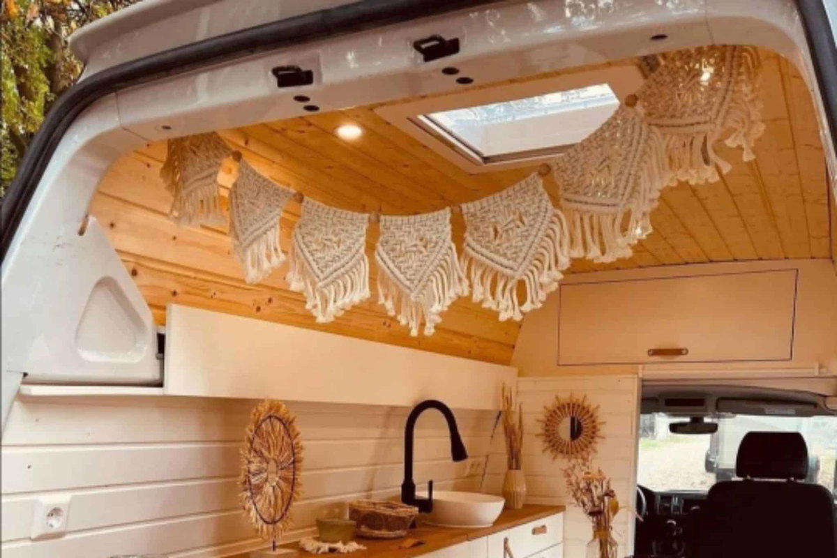 Helle, moderne Camperküche mit Holzinterieur, Makramee-Dekoration und Dachfenster für Licht und Luft.