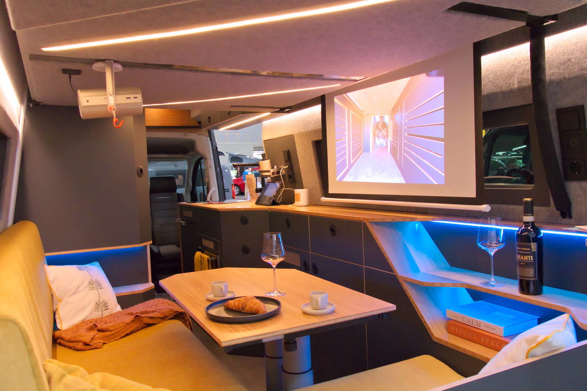 Camper Schmiede auf dem Caravan Salon 2026: Sitzgruppe mit Beamer und Leinwand.